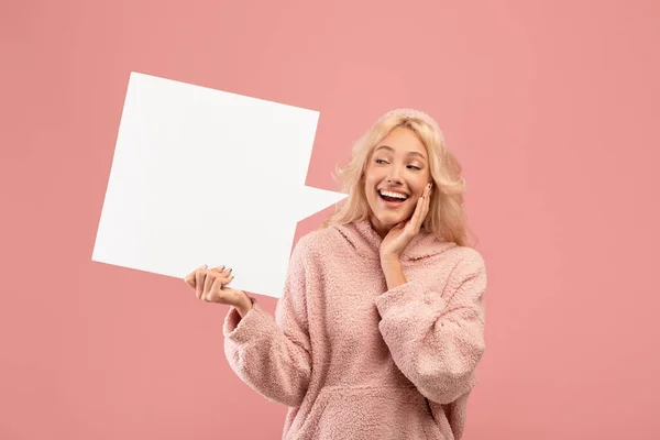 Överlycklig ung kvinna håller och tittar på tomma tal bubbla, poserar på rosa studio bakgrund, mockup — Stockfoto