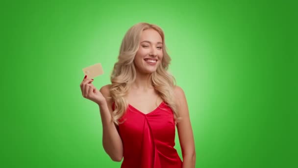 Vrolijke blonde vrouw met gouden creditcard over groene achtergrond — Stockvideo