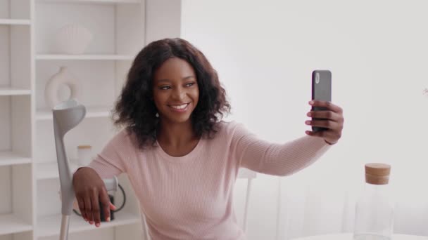 Negro dama con muletas haciendo selfie en teléfono en casa — Vídeo de stock