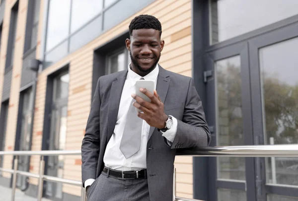 Glad svart affärsman med smartphone i handen läsa bra budskap och chatta om affären utomhus — Stockfoto