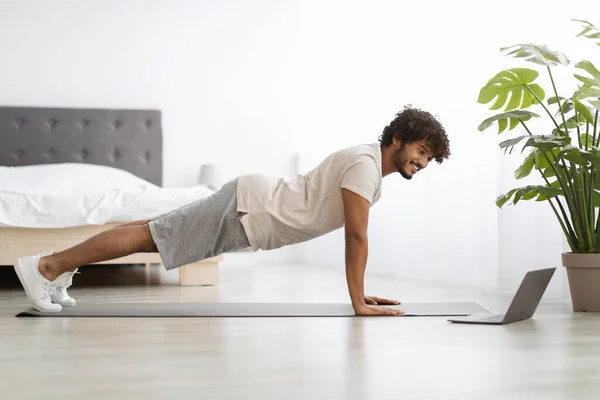 Happy athletic hindu man planking στο σπίτι, χρησιμοποιώντας φορητό υπολογιστή — Φωτογραφία Αρχείου
