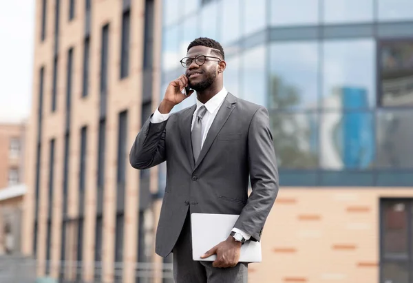 Впевнений афроамериканський підприємець з ноутбуком спілкується під час прогулянки по діловому центру. — стокове фото