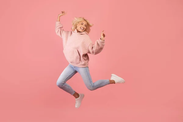 Succesvol moment. Opgewonden jonge dame springen en plezier hebben, in goed humeur, triomf vieren, roze achtergrond — Stockfoto