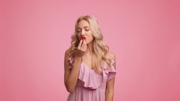 Linda senhora loira comendo morango sorrindo posando sobre fundo rosa — Vídeo de Stock
