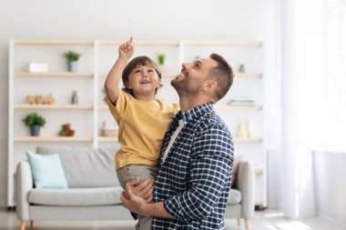 Baba, yukarı bak. Heyecanlı küçük çocuk babasıyla yukarıya bakıyor, çocuğu parmağıyla işaret ediyor, çocuğu elinde tutuyor.