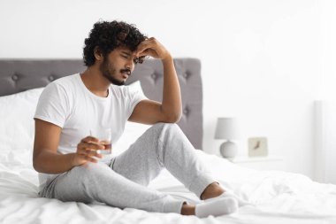 Hüsrana uğramış Hintli adam alkol içiyor, yatakta oturuyor, fotokopi çekiyor.