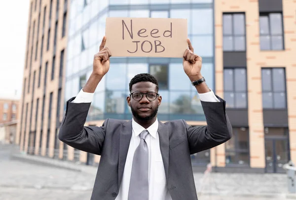 Behöver jobbkoncept. Afroamerikansk kontorsarbetare som håller affisch medan han sitter utomhus nära kontorshotell — Stockfoto
