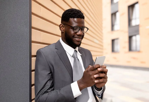 Affärskommunikation. Glad svart affärsman messar på smartphone när du går utomhus under pausen — Stockfoto