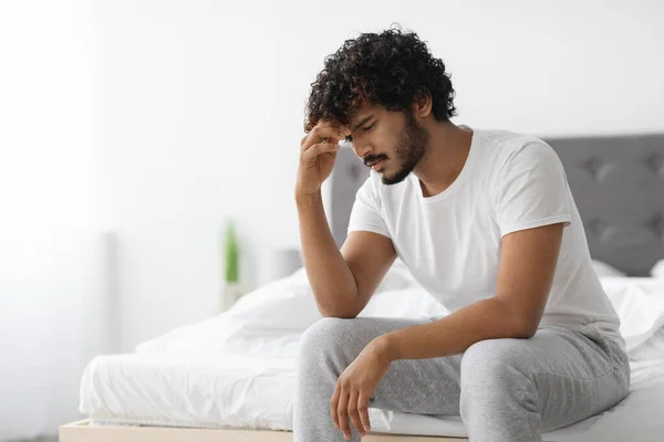Frustrated indian guy in pajamas sitting on bed — Stock Photo, Image