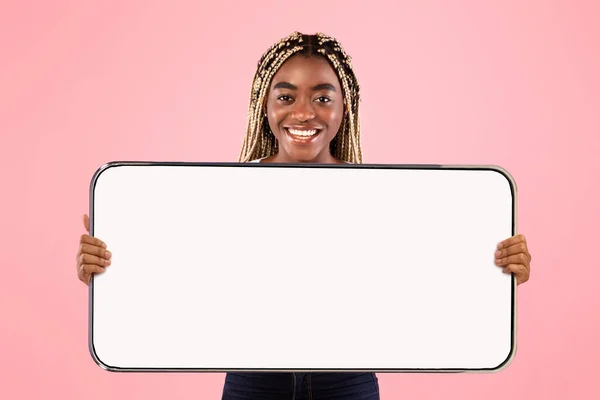 Veselý černošky dáma ukazuje velký bílý prázdný smartphone obrazovce — Stock fotografie
