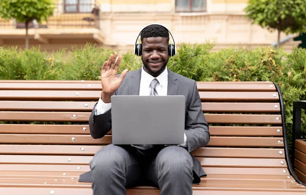 Αυτοπεποίθηση αφροαμερικανός επιχειρηματίας που έχει βιντεοκλήση στο laptop, επικοινωνία σε απευθείας σύνδεση σε εξωτερικούς χώρους, κάθεται στον πάγκο — Φωτογραφία Αρχείου