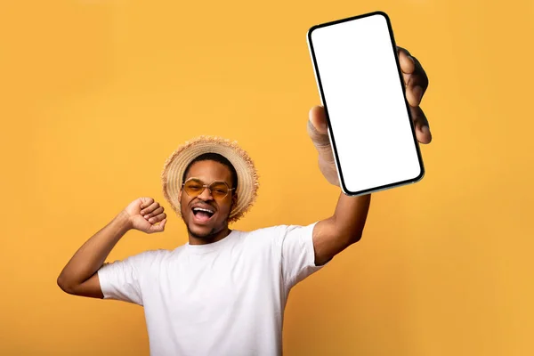 선글라스와 지푸라기 모자를 쓴 잘생긴 흑인 이 모바일 앱이나 웹 사이트 디자인을 위해 흉내를 내는 스마트폰을 보여 주고 있다. — 스톡 사진