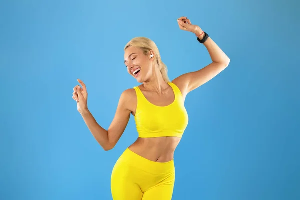 Mujer joven sonriente en ropa deportiva escuchando música y bailando — Foto de Stock