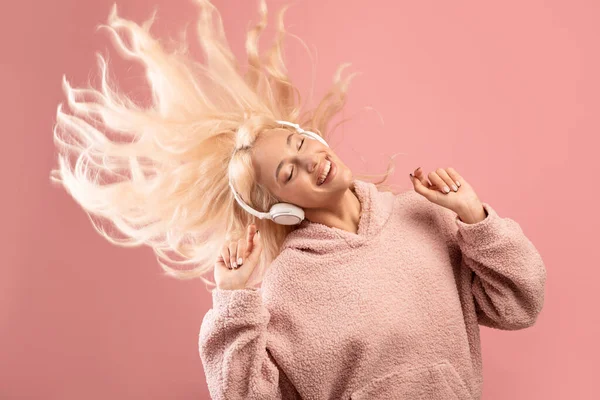 Profitez du concept musical. Joyeuse dame écoutant de la musique dans les écouteurs et dansant, jouant avec les cheveux, fond rose — Photo