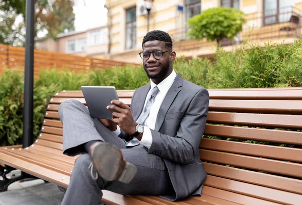 Entrepreneur afro-américain confiant à l'aide d'une tablette numérique, navigation nouvelles tout en étant assis sur le banc à l'extérieur — Photo