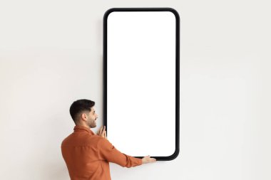 Genç Arap adam boş ekran ile büyük bir akıllı telefon gösterisi yapıyor, mobil uygulama veya web sitesi tasarımı için model öneriyor.