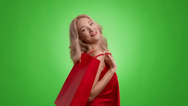 Щаслива блондинка тримає сумку для покупок, позуючи на зеленому тлі — стокове фото