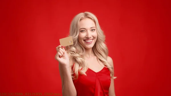Ευτυχισμένη ξανθιά κυρία κρατώντας πιστωτική κάρτα Winking Eye, κόκκινο φόντο — Φωτογραφία Αρχείου