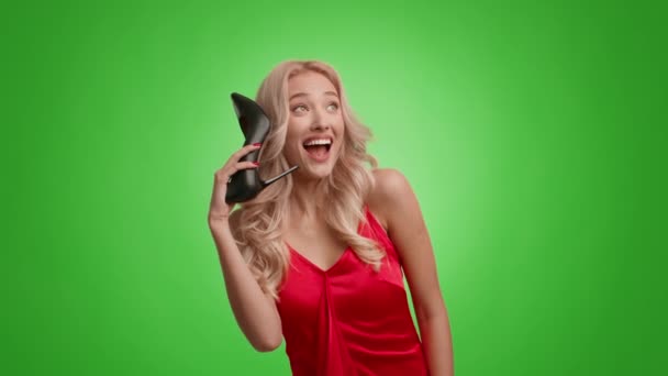 Blondine Lady Doen alsof Praten op telefoon Holding Shoe, Groene achtergrond — Stockvideo