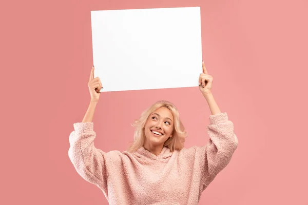 Lächelnde Dame mit leerem Brett für Werbung oder Text über dem Kopf, auf rosa Hintergrund stehend, Kopierraum — Stockfoto