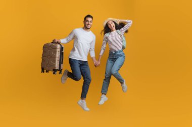 Aktif Seyahat Konsepti. Sarı arka planda bavulla atlayan neşeli bir Arap çift.