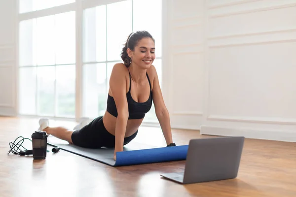 Young woman stretching back on mat with pc — Stock Photo, Image