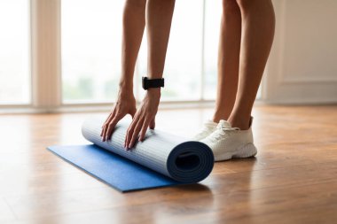 Yerde yoga minderini açan genç kadının yakın çekimi.