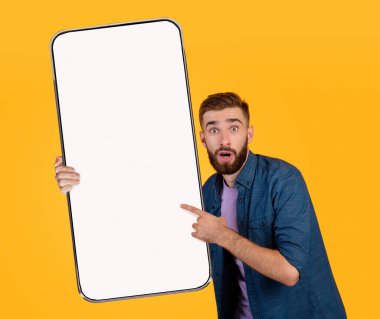 Şok edici bir teklif. Büyük boş akıllı telefonu tutan ve işaret eden heyecanlı genç adam.