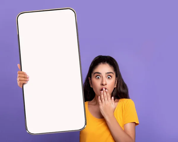 Překvapený zmatený mladý arab dáma zakrývá ústa rukou, ukazuje velký smartphone s prázdnou obrazovkou — Stock fotografie