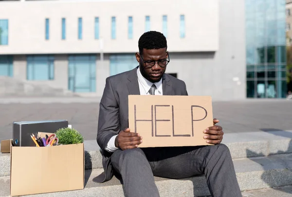 Olycklig förtvivlad svart affärsman förlorade jobbet håller plakat med ord HJÄLP, sitter på trappor nära business center — Stockfoto