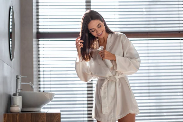 Haarverzorging Cosmetisch. Mooie Millennial vrouw toepassen vochtinbrengende haarspray in de badkamer — Stockfoto