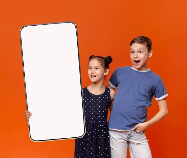 Emocionado niño y niña sosteniendo Smartphone en blanco con pantalla blanca para burla —  Fotos de Stock