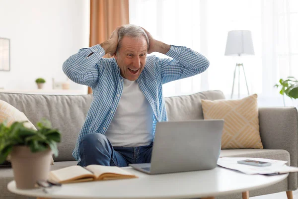 Зрілий чоловік використовує ноутбук, святкуючи успіх вдома — стокове фото