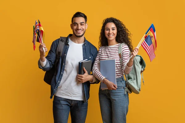 Istruzione all'estero. Giovane arabo uomo e donna holding pila di bandiere internazionali — Foto Stock