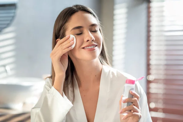 Bella donna sorridente pelle detergente con acqua micellare e batuffolo di cotone — Foto Stock