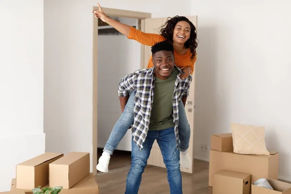 Vrolijke zwarte man dragen vrouw iggyback verhuizen naar nieuw huis — Stockfoto