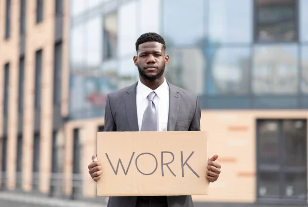 Concepto de desempleo. Hombre de negocios afroamericano en traje sosteniendo cartel con palabra TRABAJO, de pie al aire libre — Foto de Stock