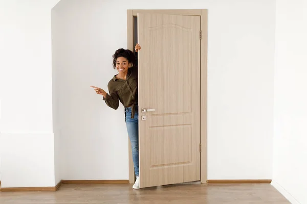 Feliz dama africana abriendo la puerta señalando dedo aparte de pie en el interior — Foto de Stock