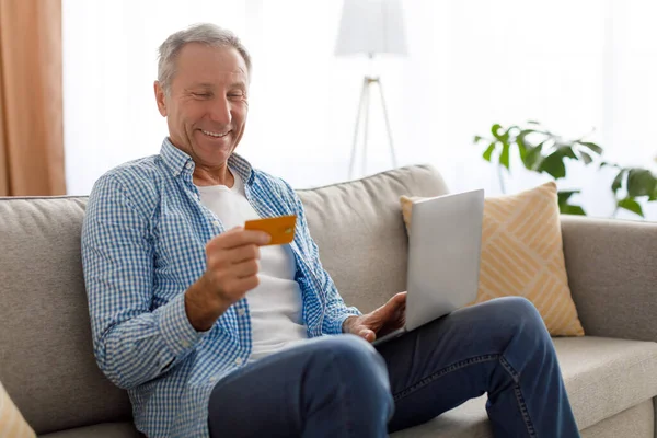 Χαμογελώντας ώριμος άνθρωπος χρησιμοποιώντας υπολογιστή και πιστωτική κάρτα στο σπίτι — Φωτογραφία Αρχείου