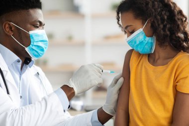 Afrikalı Amerikalı doktor genç kız için aşı yapıyor.
