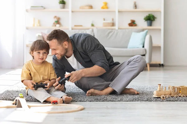 Η ιδέα των βιντεοπαιχνιδιών. Χαριτωμένο μικρό αγόρι παίζει στο gamepad με τον μπαμπά, κάθεται στο πάτωμα στο σπίτι και συγκόλληση, κενό χώρο — Φωτογραφία Αρχείου