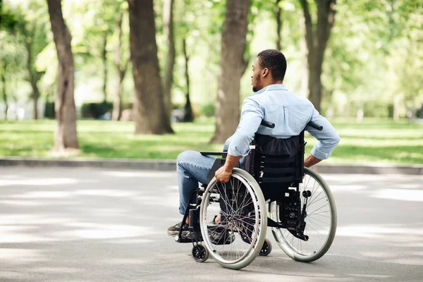 Bedachtzame jonge zwarte man in een rolstoel wandelen in het stadspark, kopiëren ruimte — Stockfoto