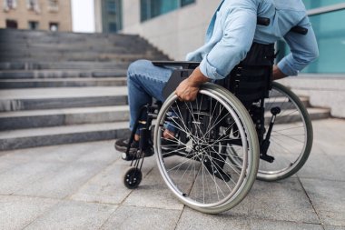 Tekerlekli sandalyedeki genç siyahi adamın merdivenlerin önünde rampası olmadan, binaya girme ihtimali olmadan yakın plan çekimleri.