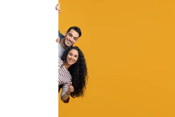 Ευτυχισμένος Άραβας άνδρας και γυναίκα κρυφοκοιτάζει πίσω από το μεγάλο λευκό πίνακα διαφήμισης — Φωτογραφία Αρχείου