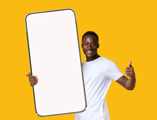 Chico negro mostrando la pantalla grande del teléfono inteligente blanco vacío y como —  Fotos de Stock