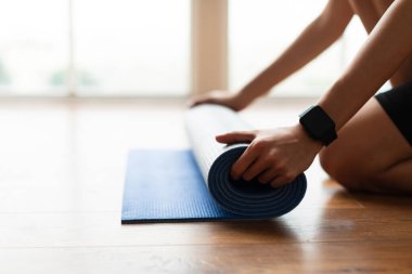 Genç bir kadın yoga minderini yere seriyor.