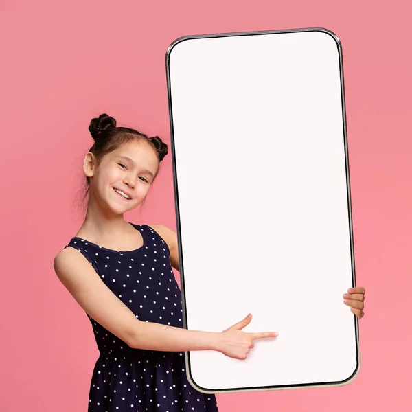 Linda chica preadolescente apuntando a Smartphone grande con pantalla blanca en blanco — Foto de Stock