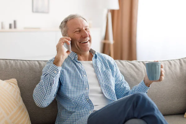 Веселый взрослый мужчина разговаривает по телефону, сидя на диване — стоковое фото