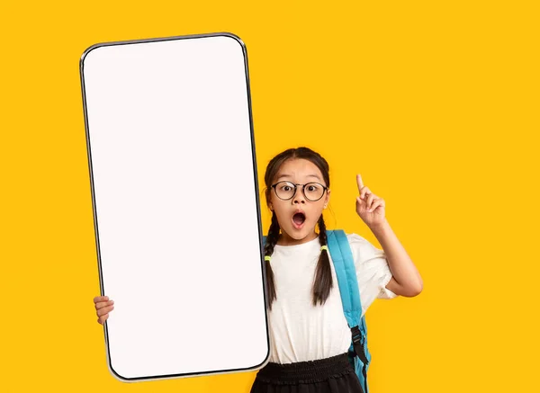 Malá školní dívka ukazující bílý prázdný smartphone obrazovku — Stock fotografie