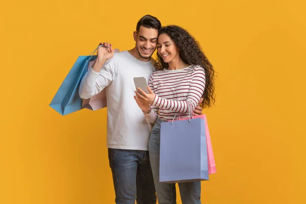 App de compras. Médio Oriente Cônjuges Segurando Shopper sacos e usando Smartphone — Fotografia de Stock